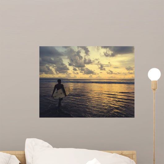 a surfer in bali beach walking toward the sunset Wall Mural