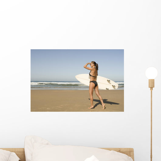 Young woman with surfboard on beach Wall Mural