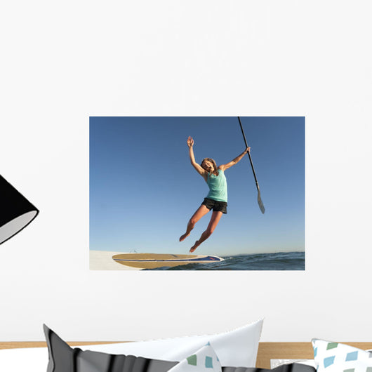 A Woman Jumps Into The Water Off A Surf Board While Holding Her Paddle Wall Mural