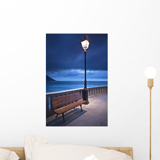 A Bench And Light Post Along The Railing On The Coast Wall Mural