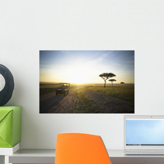A Vehicle Drives Down A Dirt Road At Sunset Wall Mural