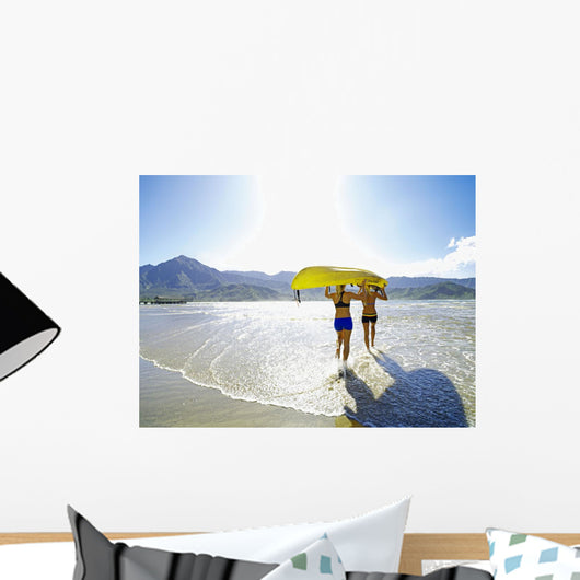 Two Active Young Woman Carrying A Kayak Into The Ocean Wall Mural