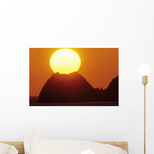 Sun Setting In Orange Sky Over Ocean And Silhouetted Hill Wall Mural