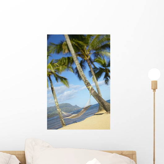 Hammock tied between palm trees on sandy beach Wall Mural