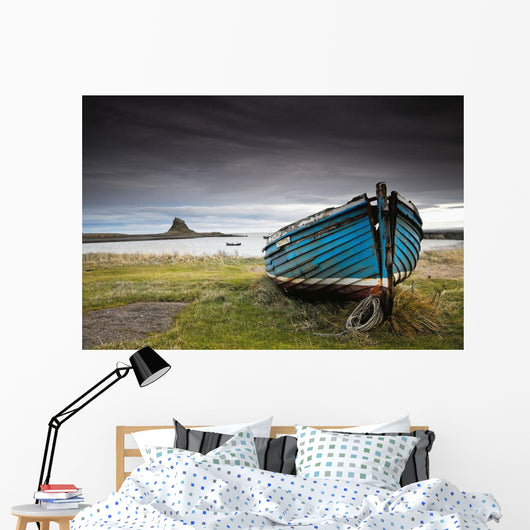 A Weathered Boat Sitting On The Shore With Lindisfarne Castle Wall Mural