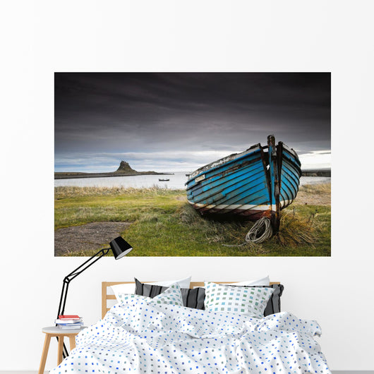 A Weathered Boat Sitting On The Shore With Lindisfarne Castle Wall Mural