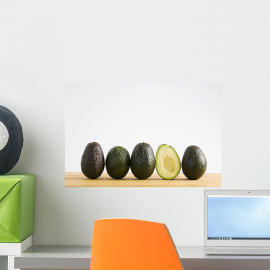 A Row Of Avocados Standing Upright On A Wooden Board With One Cut Wall Mural