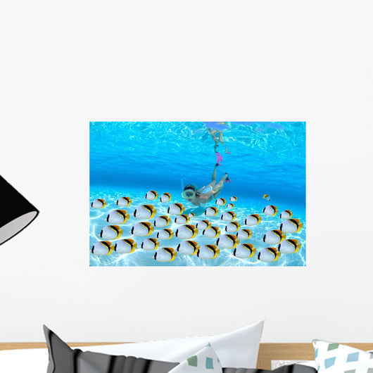 Woman snorkeler near sandy bottom, Butterflyfish school foreground Wall Mural