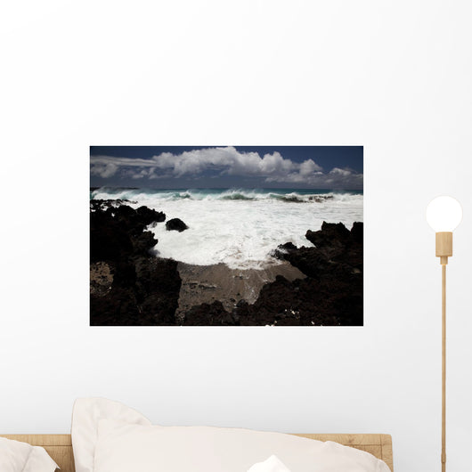 A wave breaks with lave rocks in the foreground Wall Mural