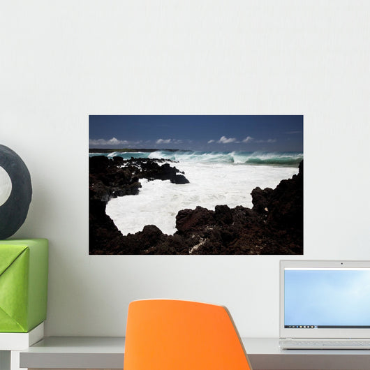 A wave breaks with lave rocks in the foreground Wall Mural