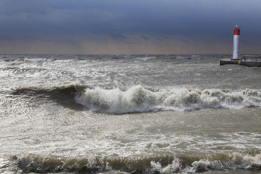 Storm waves crashing on a beach near a lighthouse on lake ontario Wall Mural