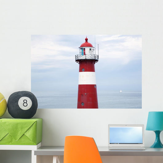Red and white lighthouse along the coast with a sailboat Wall Mural