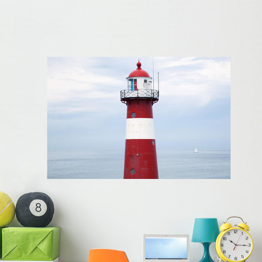 Red and white lighthouse along the coast with a sailboat Wall Mural