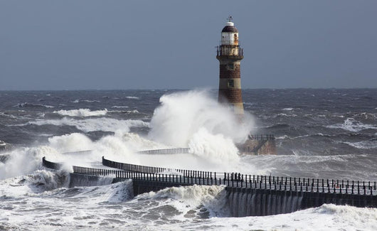 Waves crashing into a lighthouse Wall Mural