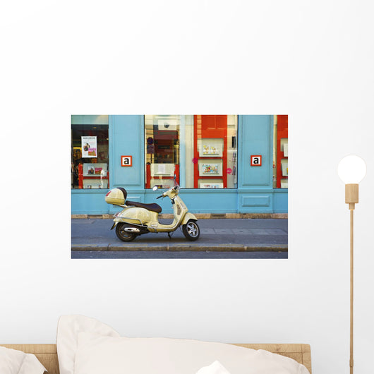 A motorized scooter parked outside a blue building along a street Wall Mural