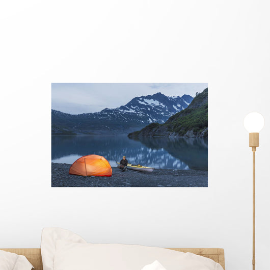 Man reading on a electronic tablet while camping with a tent and kayak Wall Mural