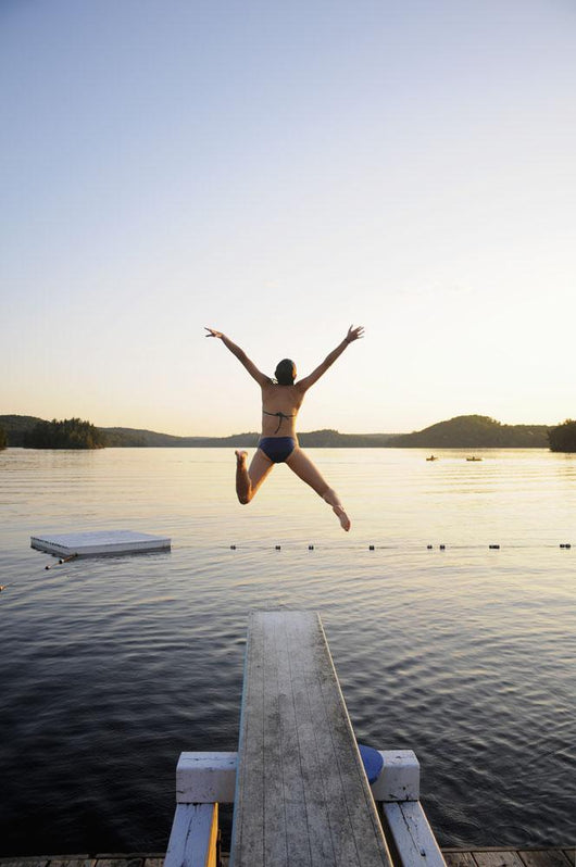 A swimmer jumps off a diving board as the sun sets over a lake Wall Mural