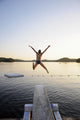 A swimmer jumps off a diving board as the sun sets over a lake Wall Mural