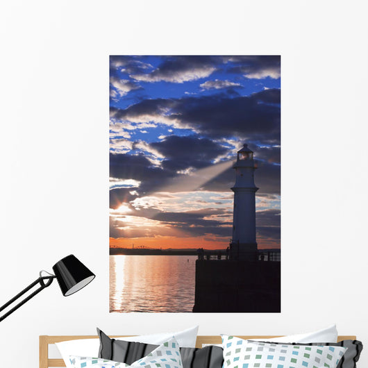 Lighthouse at sunset with light beam Wall Mural