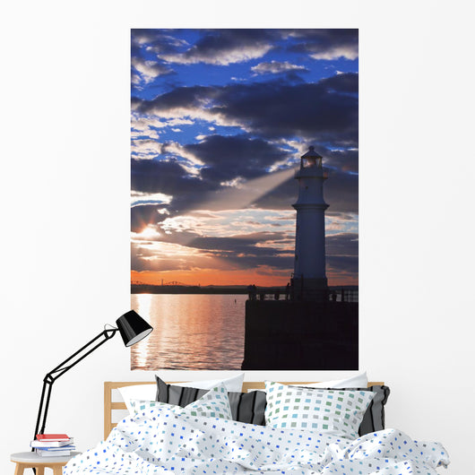 Lighthouse at sunset with light beam Wall Mural