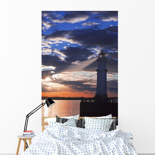 Lighthouse at sunset with light beam Wall Mural