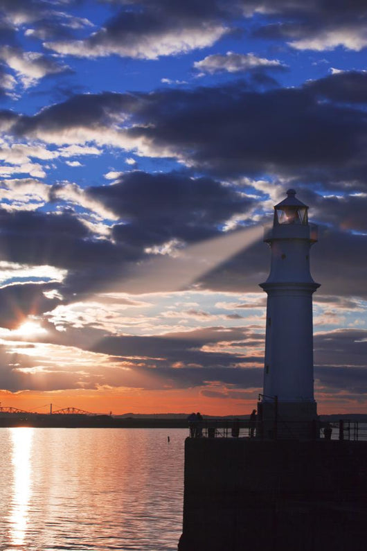 Lighthouse at sunset with light beam Wall Mural