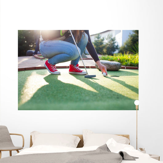 Young woman plays adventure/mini golf in summer evening Wall Mural
