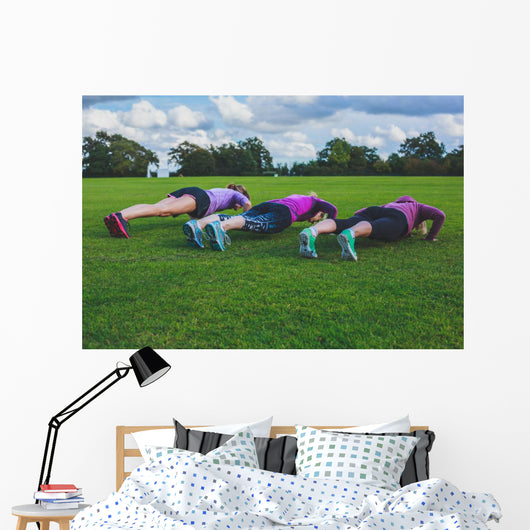 Three women doing push ups in park Wall Mural