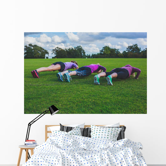 Three women doing push ups in park Wall Mural