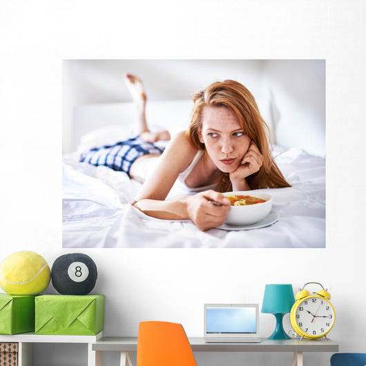 woman in bed eating chicken noodle soup while sick Wall Mural