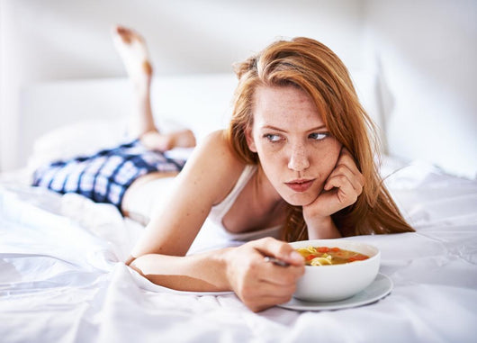 woman in bed eating chicken noodle soup while sick Wall Mural