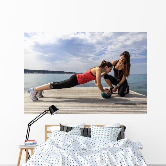 Young woman doing push-ups on a medicine ball with a coach Wall Decal