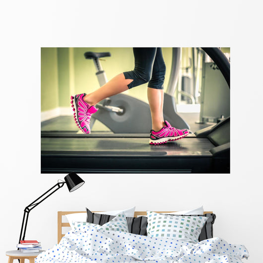 Fitness girl running on treadmill. With muscular legs in gym. Wall Mural