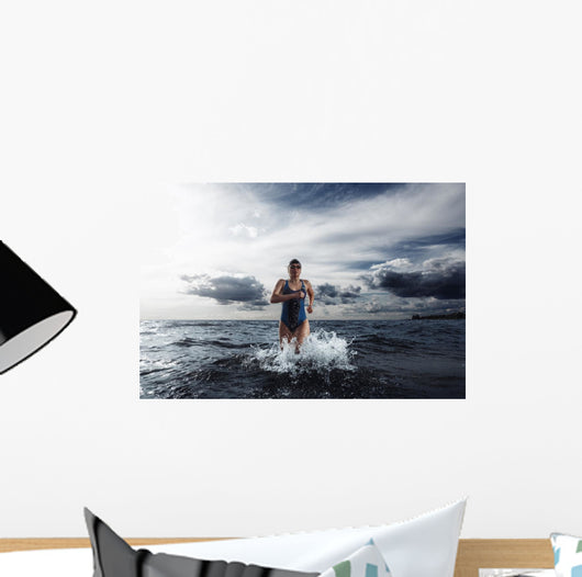 Young woman athlete running out of water Wall Mural