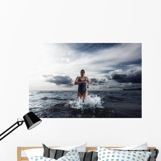 Young woman athlete running out of water Wall Mural
