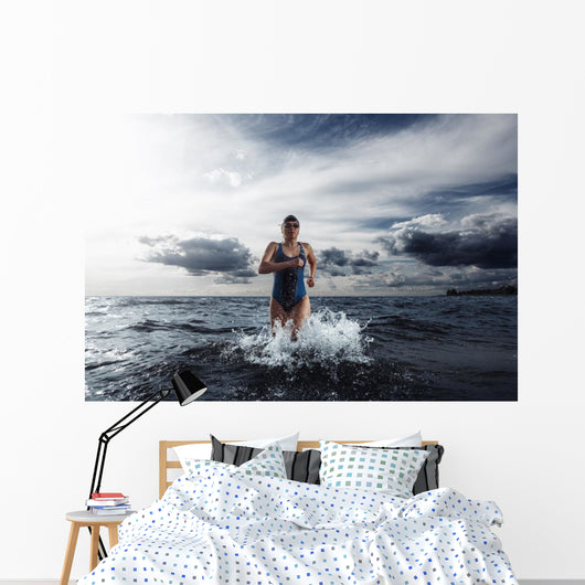 Young woman athlete running out of water Wall Mural