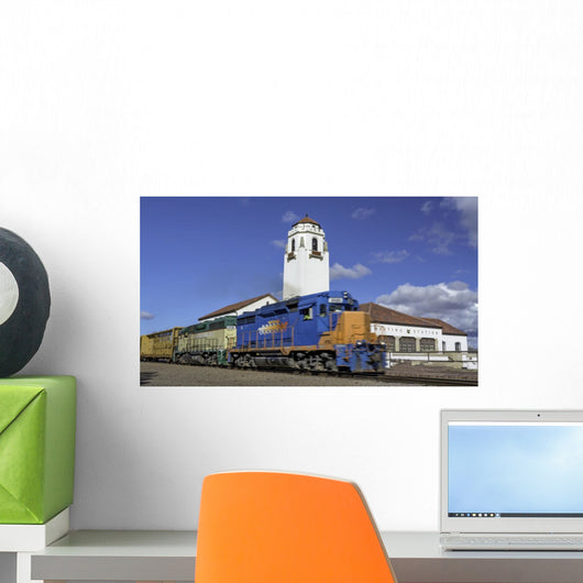 Train engine pulls its cars by the depot with blue sky Wall Mural