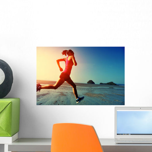 young woman running on sunrise beach Wall Mural