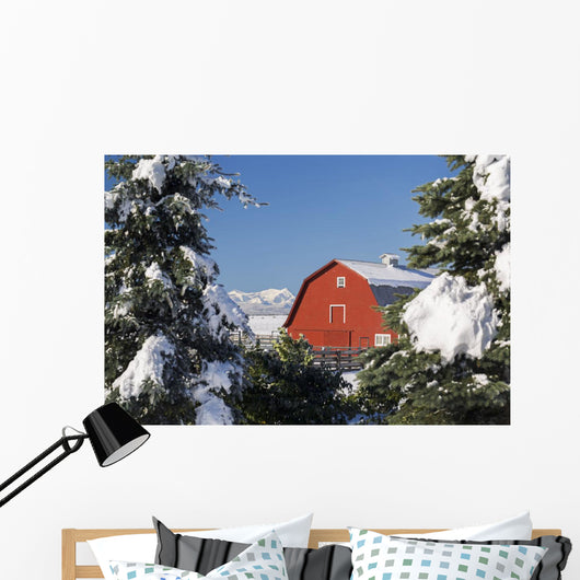 Snow covered red barn, evergreens, mountains Wall Mural