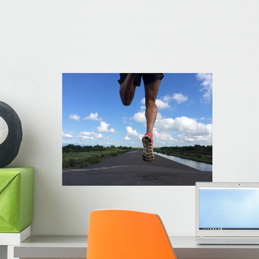 Rear view of man running and jumping down a path on blue sky day Wall Mural