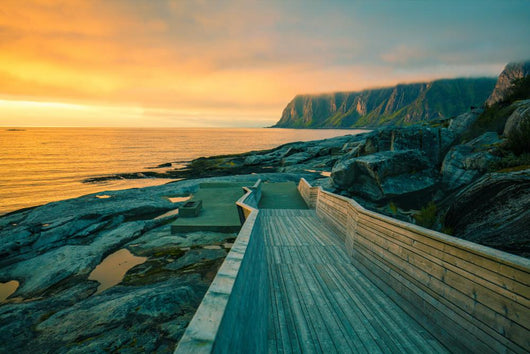 Senja island at orange sunset. Wooden pathway on the rocky beach Wall Mural