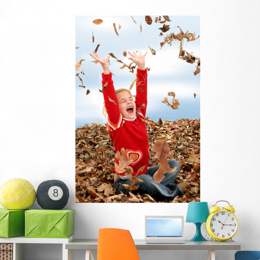happy seven year old girl playing in pile of leave Wall Mural