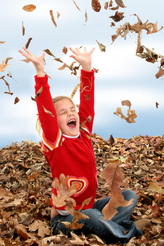 happy seven year old girl playing in pile of leave Wall Mural