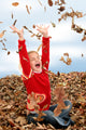 happy seven year old girl playing in pile of leave Wall Mural