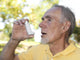 Elderly man using asthma inhaler outdoors Wall Mural