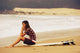 Young Woman Sitting On Her Surf Board On The Beach Wall Mural