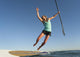 A Woman Jumps Into The Water Off A Surf Board While Holding Her Paddle Wall Mural