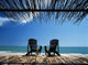 Two Chairs On Deck By Ocean Shaded By Grass Roof Wall Mural