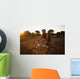 A Man Riding His Bike Through Tall Grass At Sunset Wall Mural