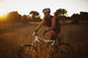 A Man Riding His Bike Through Tall Grass At Sunset Wall Mural